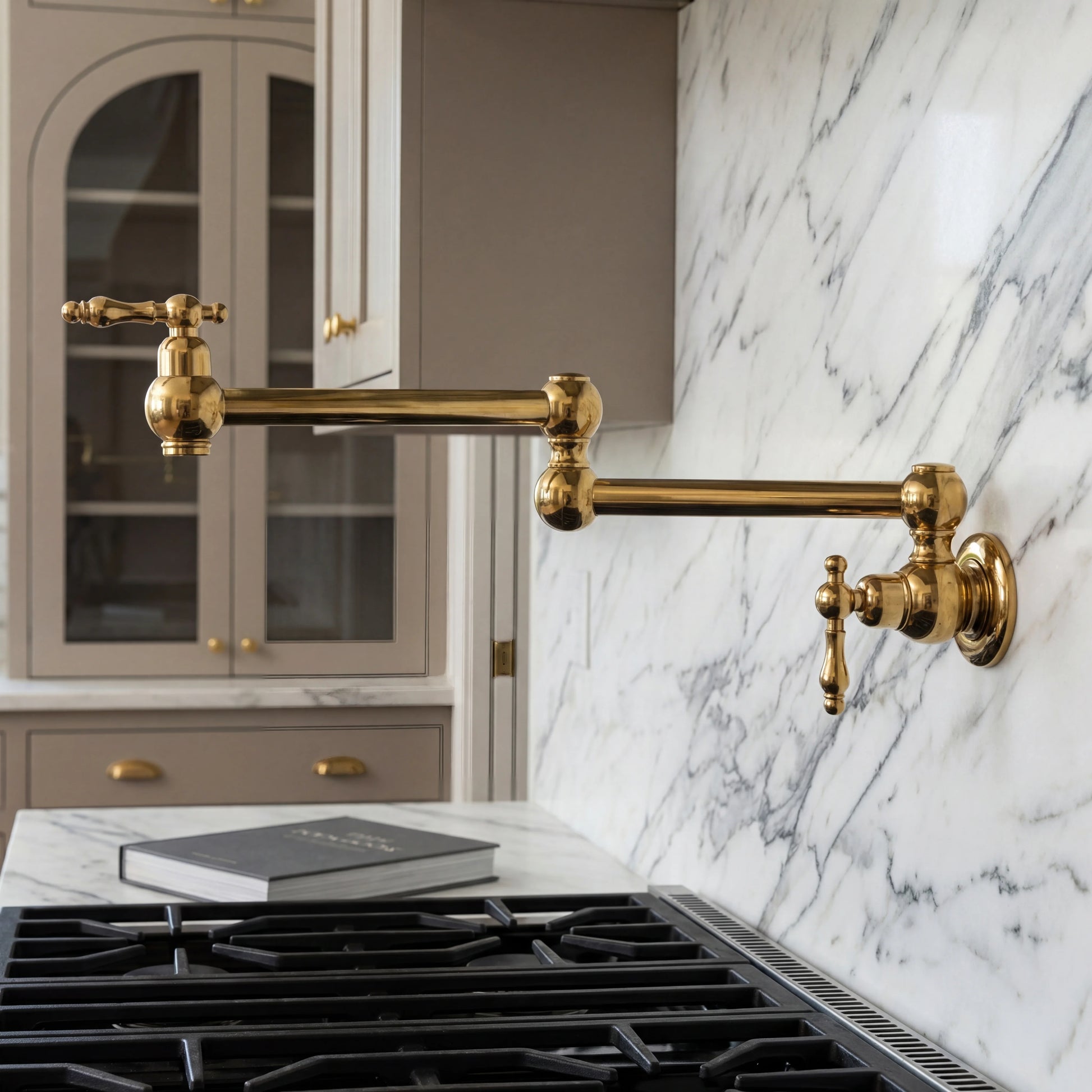 Gold kitchen faucet mounted on a marble wall above a stove with gray cabinets.