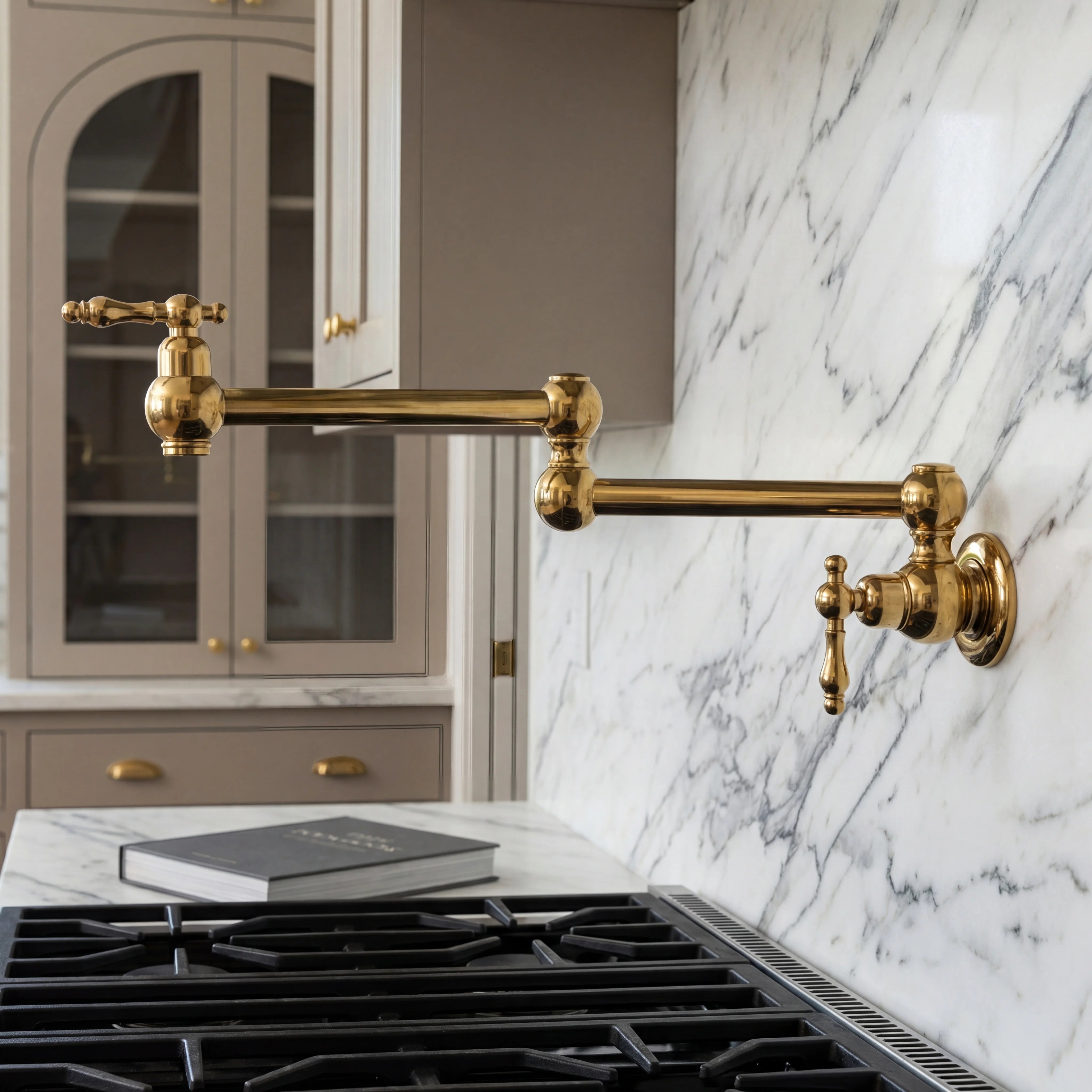 Gold kitchen faucet mounted on a marble wall above a stove with gray cabinets.