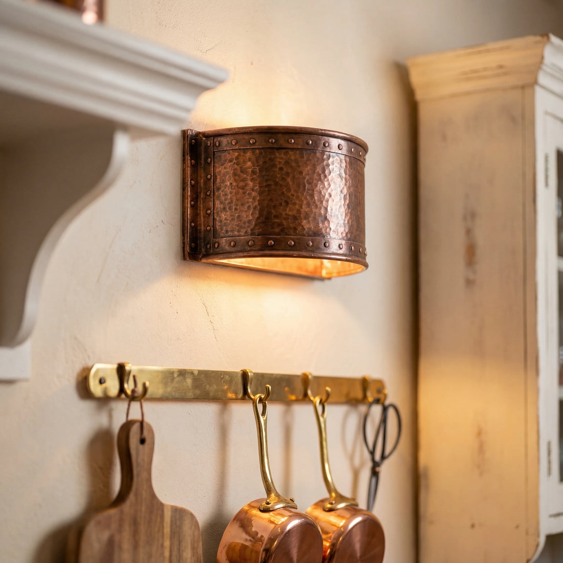 Copper pot rack with hanging pots and a wall-mounted light fixture in a kitchen setting.