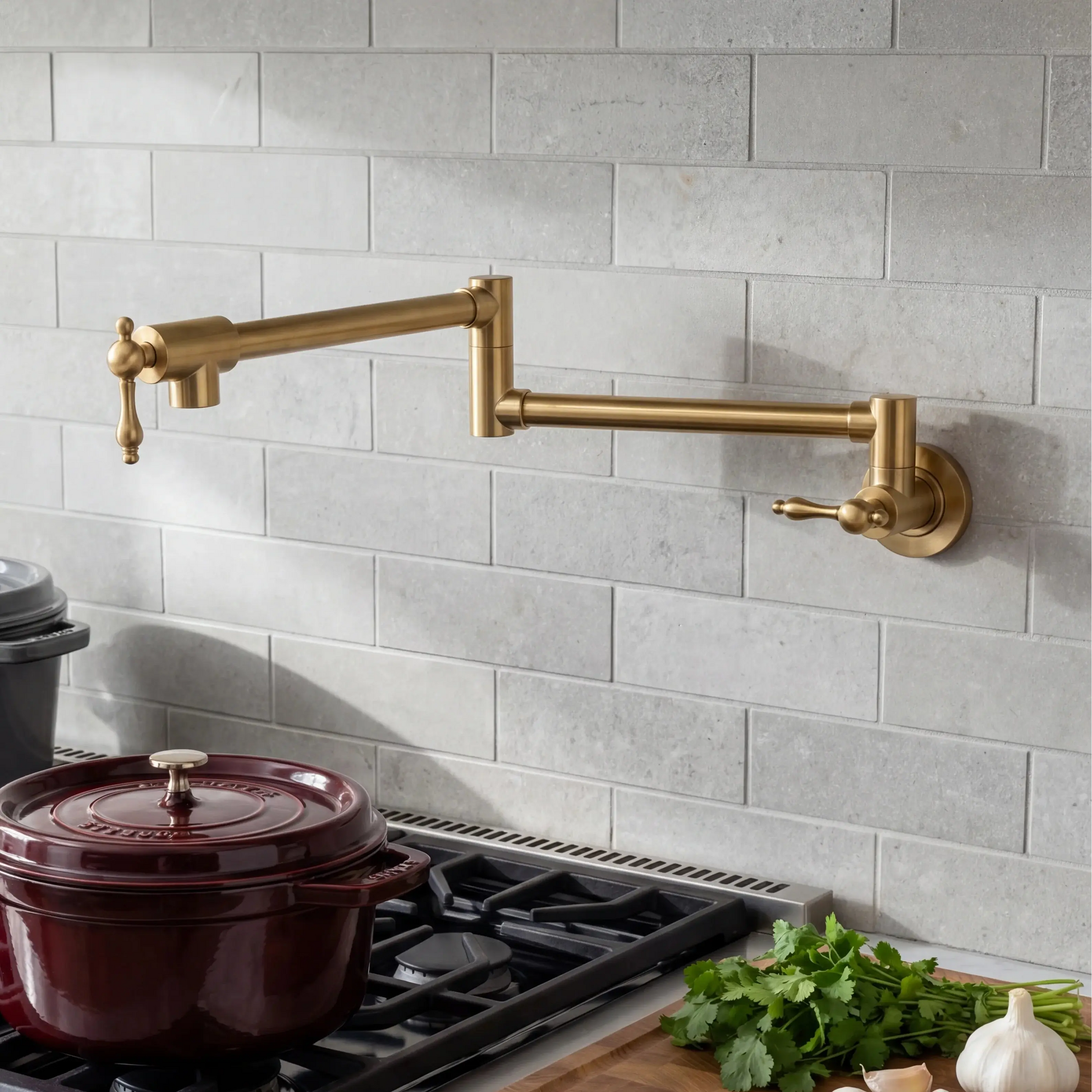 A wall-mounted brass kitchen faucet with an adjustable gooseneck spout and separate lever handle, installed on a light gray subway tile backsplash above a gas stove. A dark red enameled pot sits on the burner, with fresh parsley and garlic on the counter.